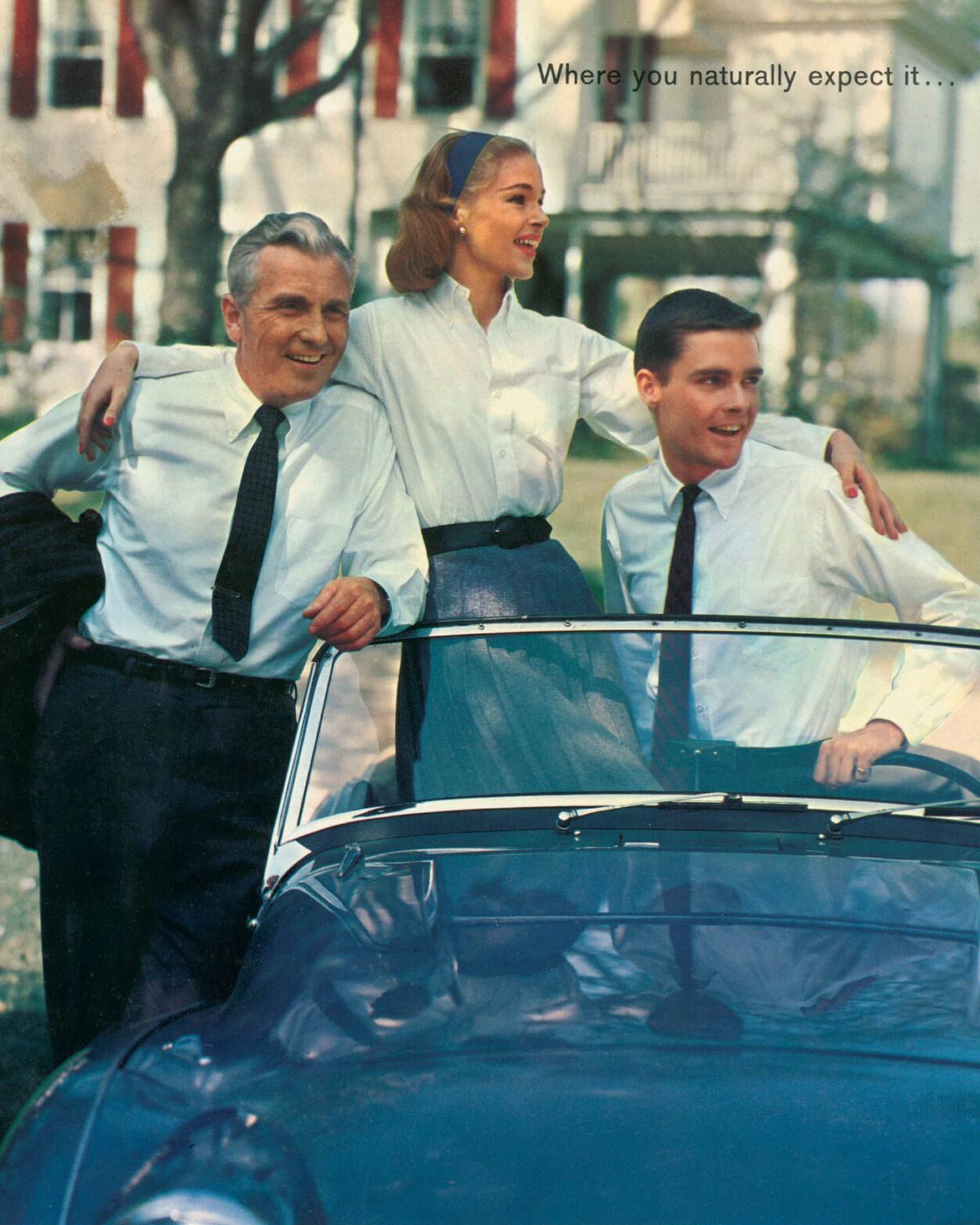 Three people in white shirts and black ties standing next to a blue convertible, with a house and trees in the background.